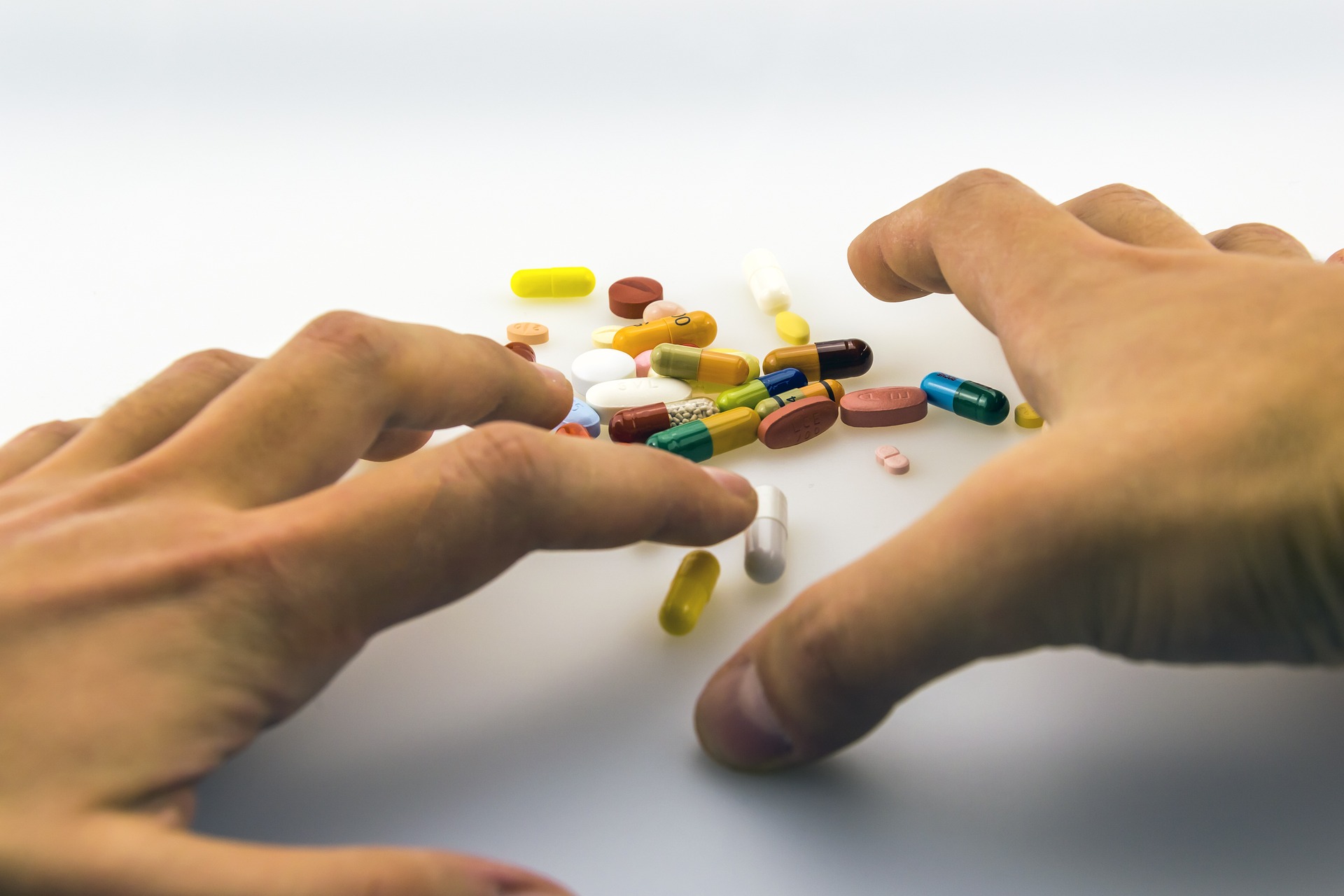 Hands of a male adult about to grab a pile of assorted medicines, some in capsules; others in tablet forms