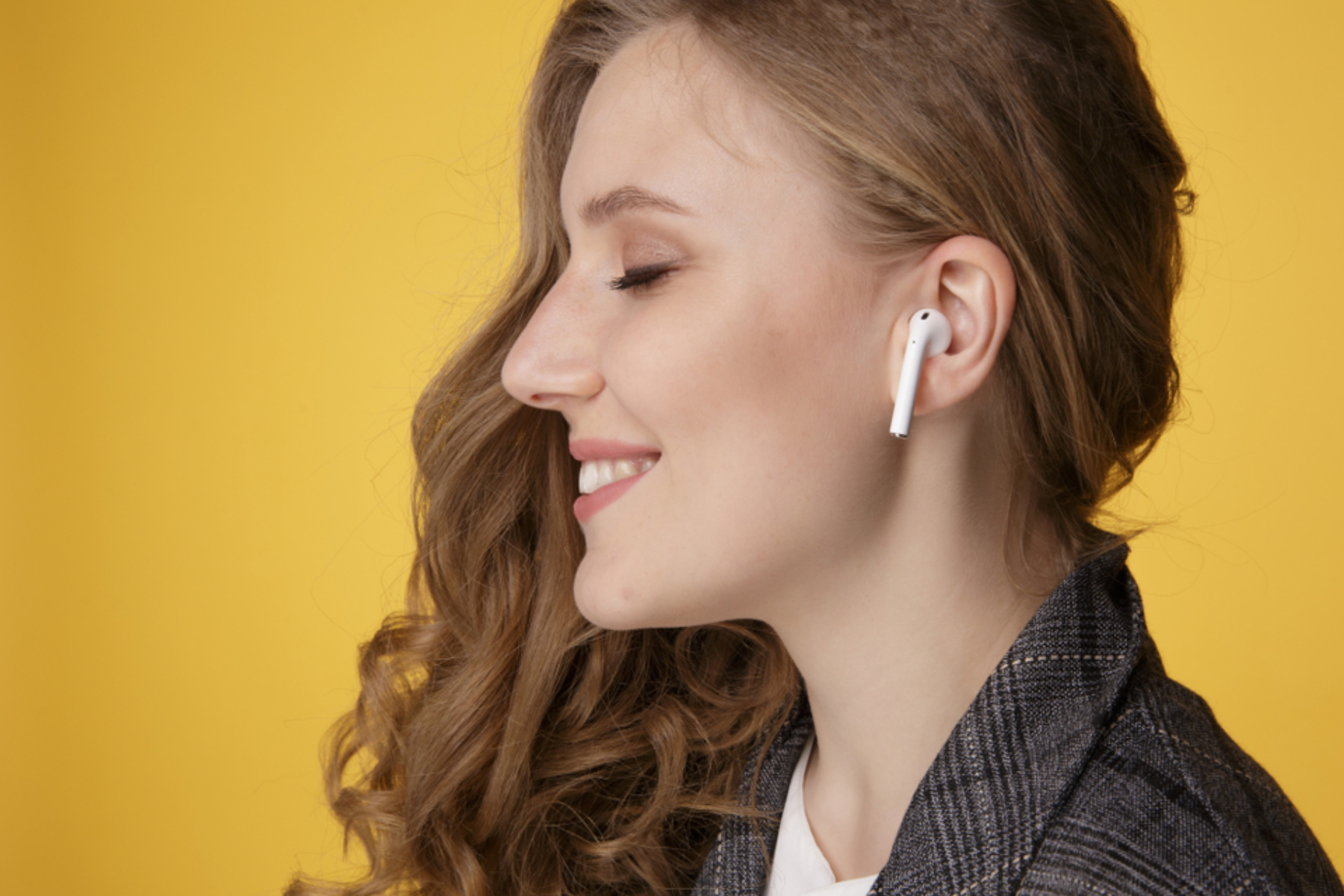 A woman wearing an airpods against a yellow background