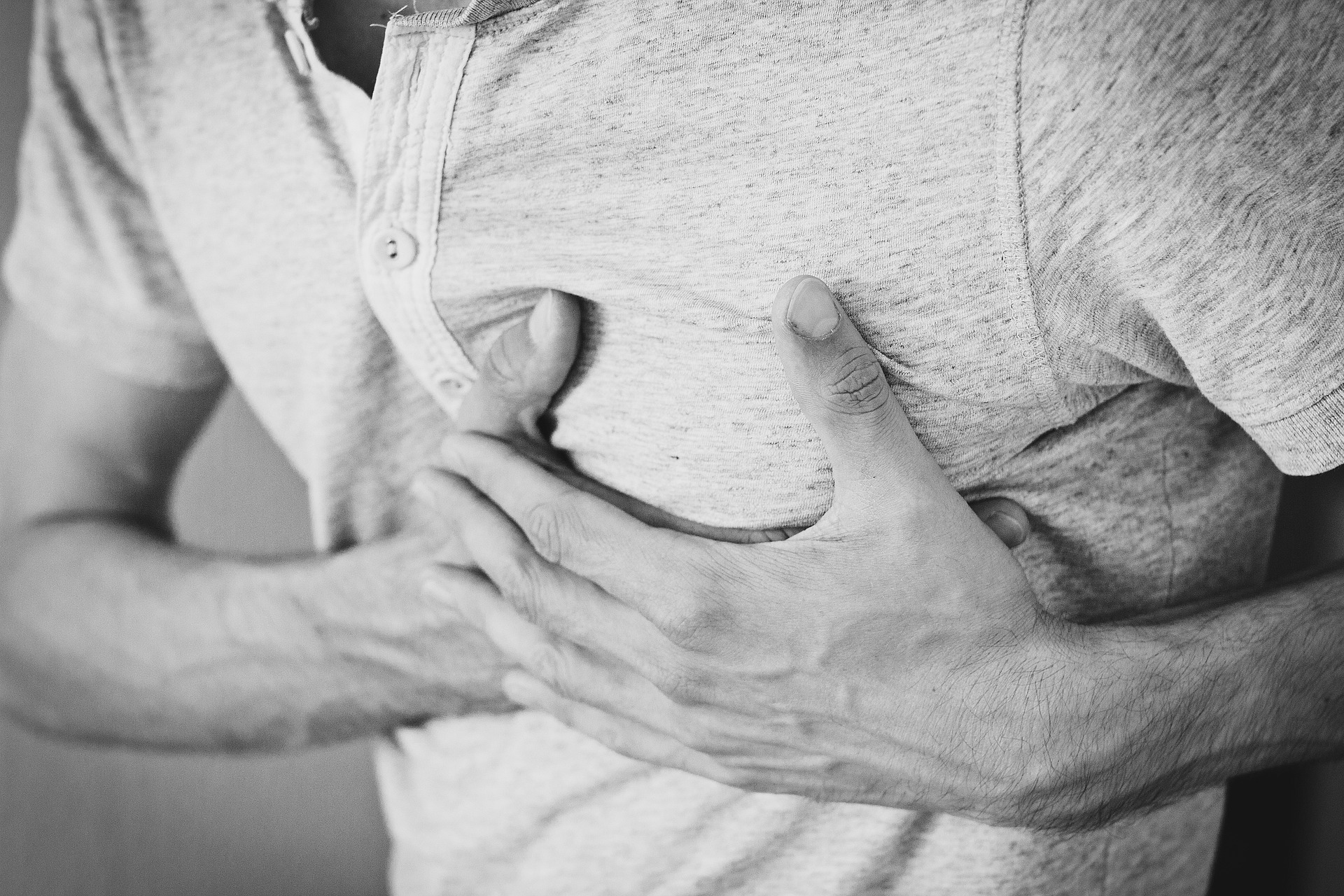 An adult male in a short-sleeved shirt with buttons touching his chest with both hands during a cardiac arrest