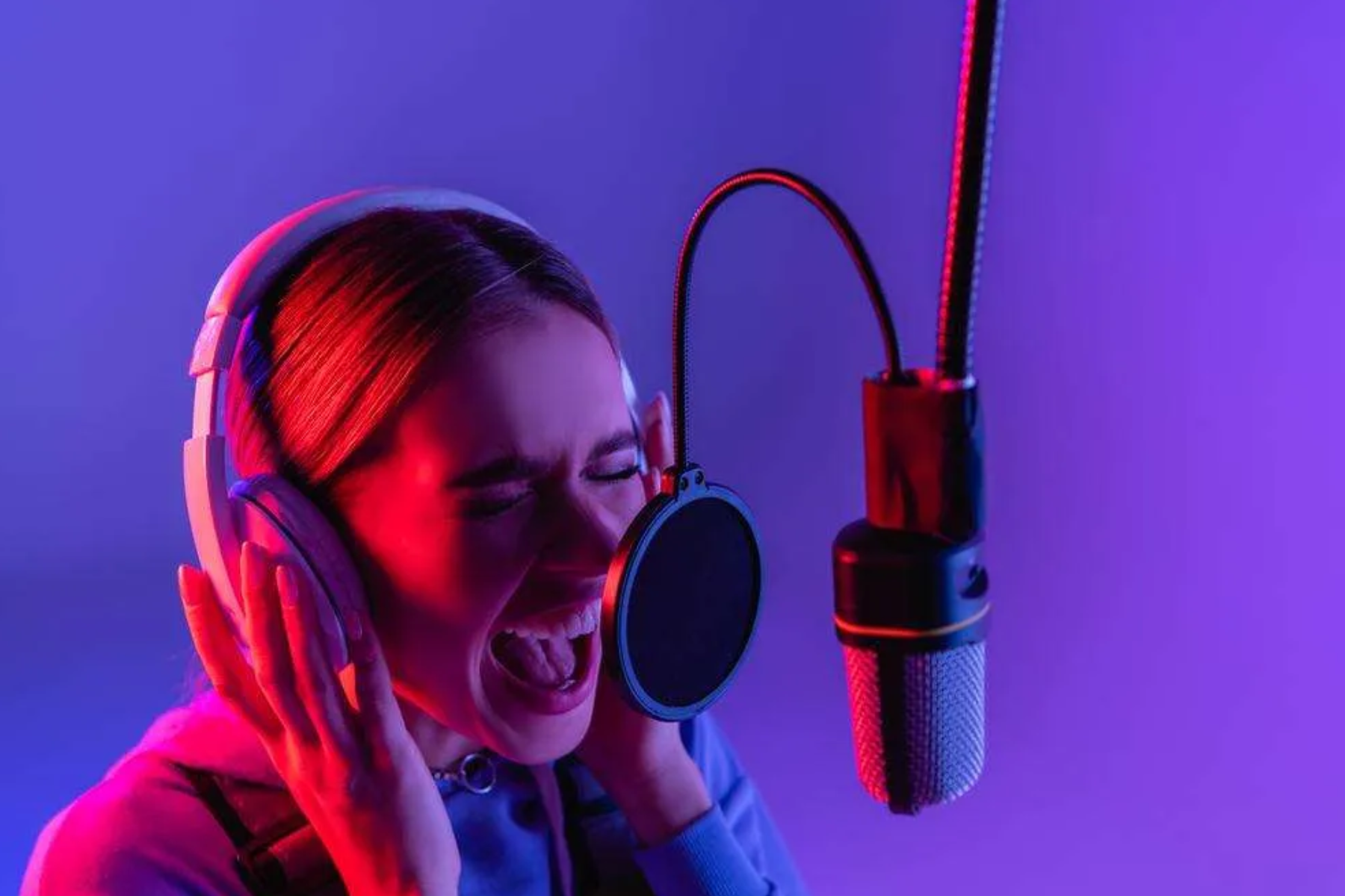 A female vocalist wearing wireless headphones singing in front of a microphone in a recording studio