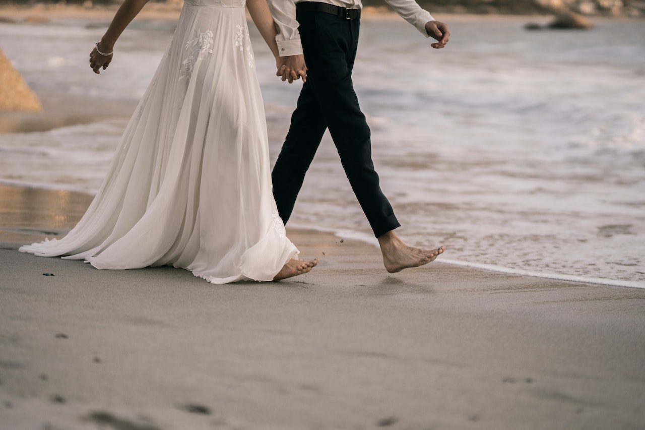 Man and Woman Walking Barefooted on Seashore Holding Hands