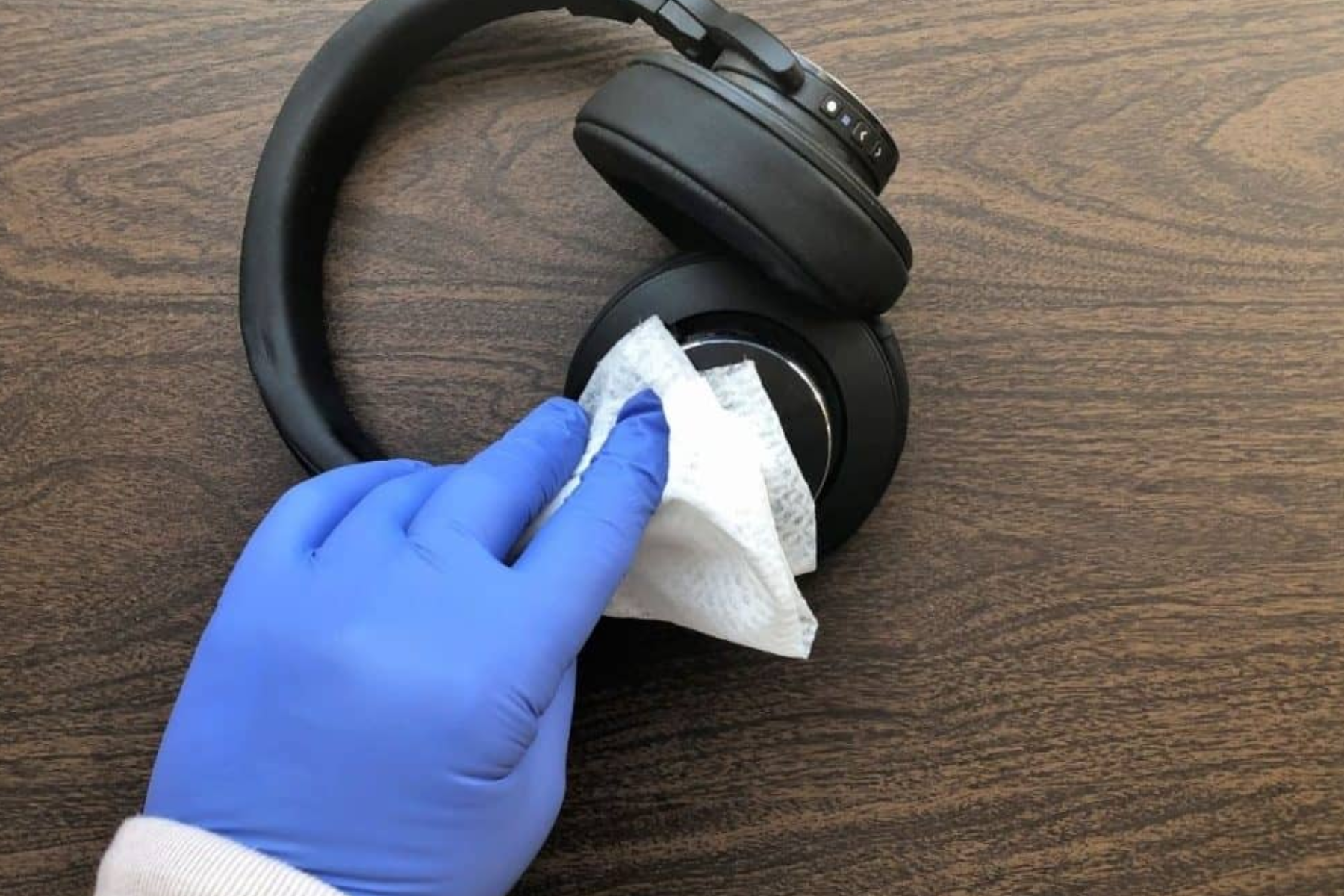 A gloved hand using a tissue to clean a headphone