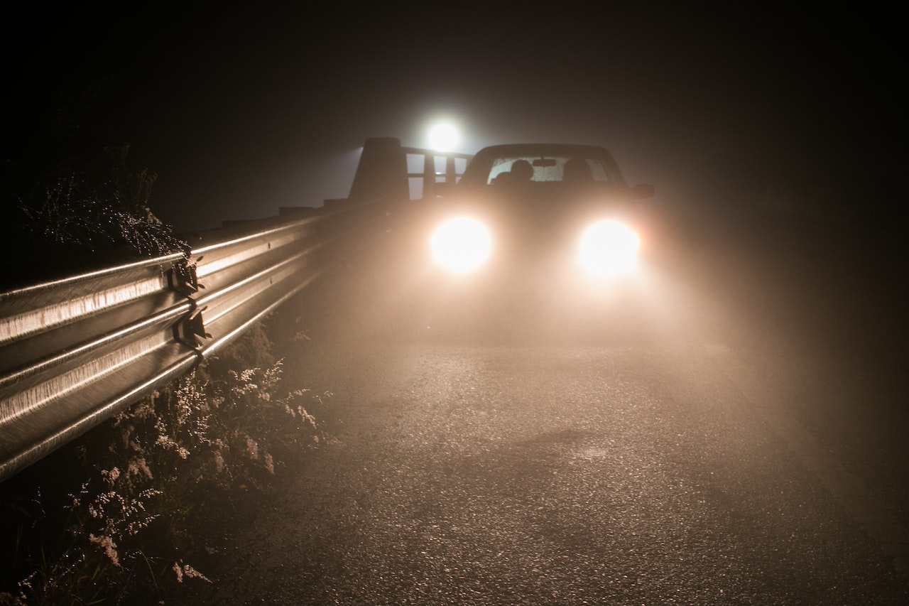 A lone car on the road with bright headlights during nighttime and another light behind it