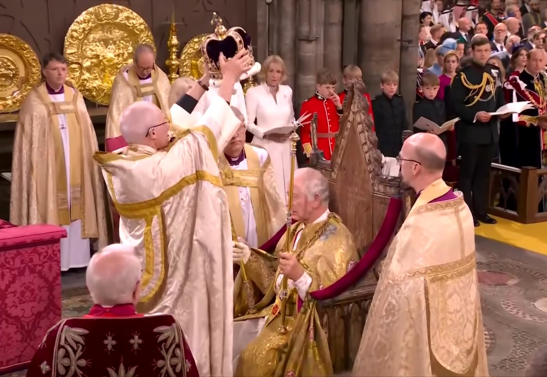The Archbishop of Canterbury holding the crown with both hands above the head of a sitting King Charles III