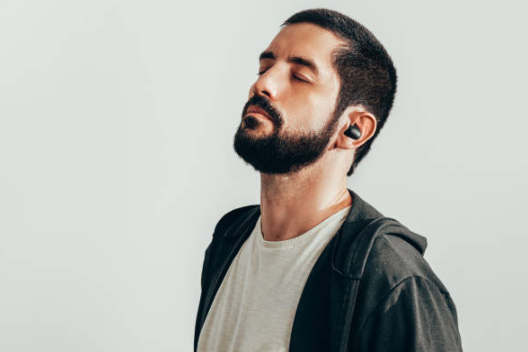 A man wearing black earbuds, closing his eyes while listening to music