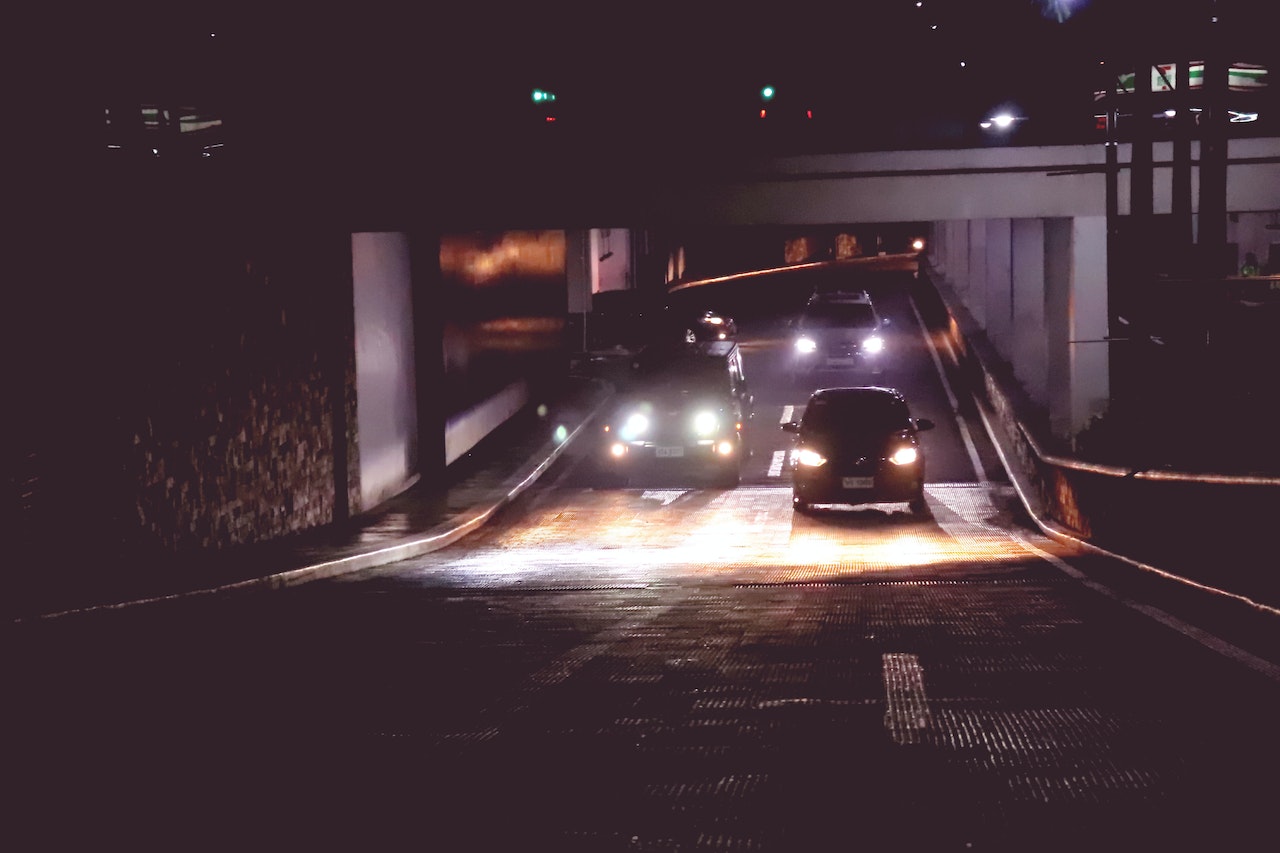 Two cars and two SUVs in a dark tunnel at nighttime with headlights on