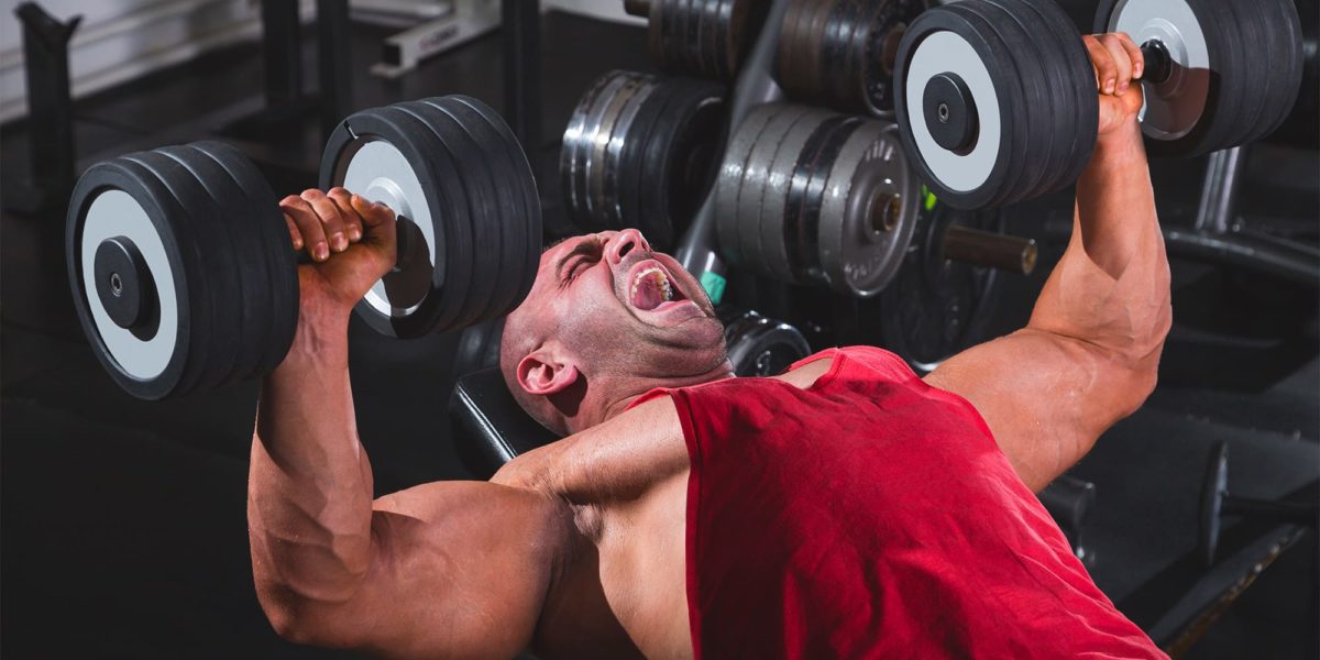 A man in a red shirt screaming while working out with dumbbells