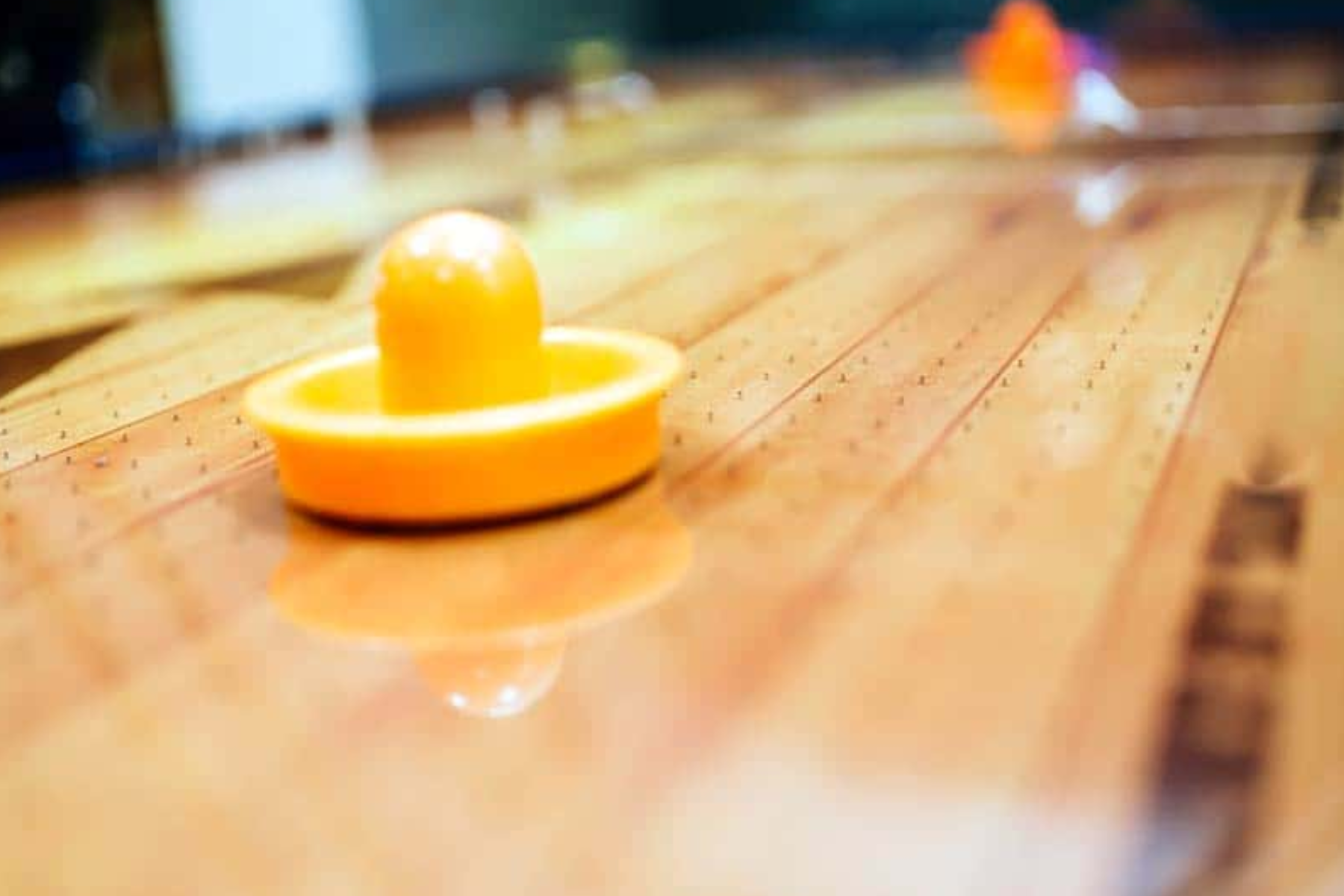 A close-up view of a yellow Air Hockey puck resting on the surface of the table