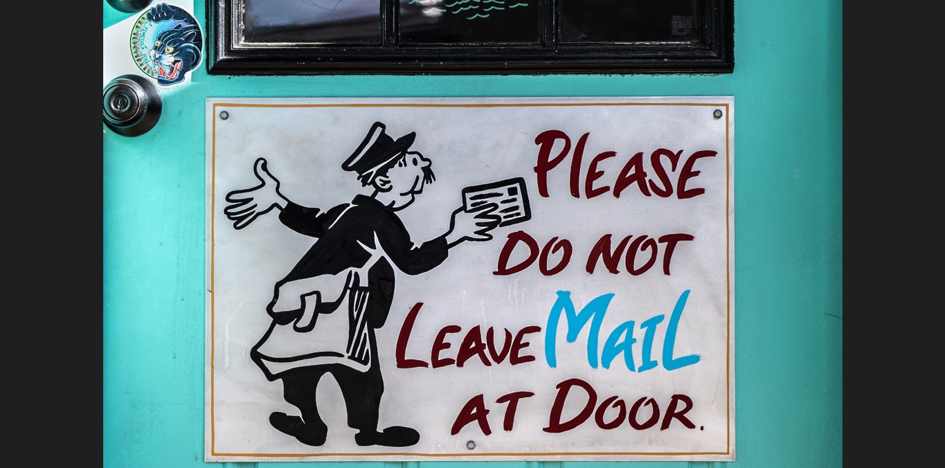 Sign with a drawn mailman at the bottom of a blue-green door that says ‘Please do not leave mail at door’
