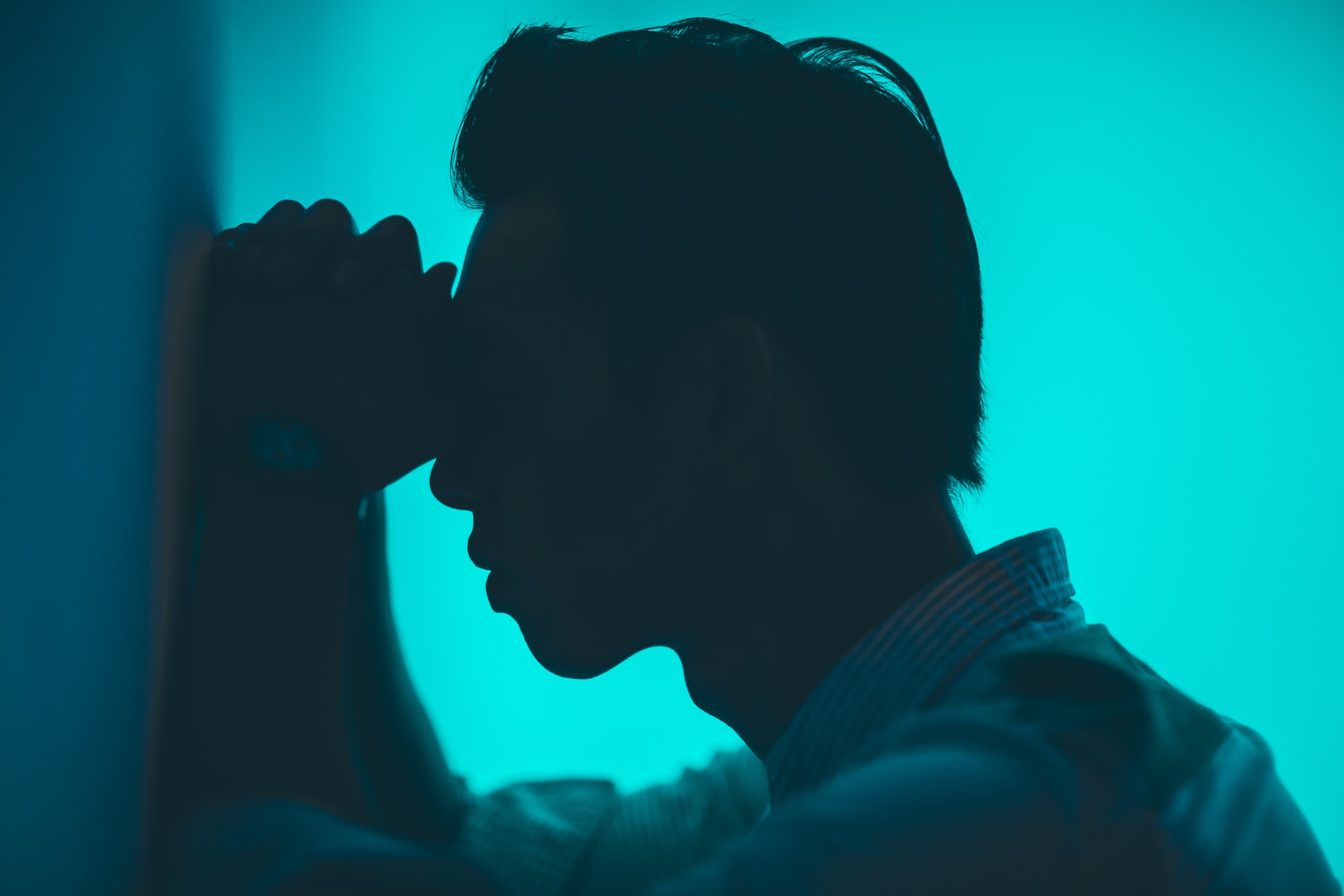 Silhouette of an adult man resting his forehead on his fists as he pushes himself on a wall