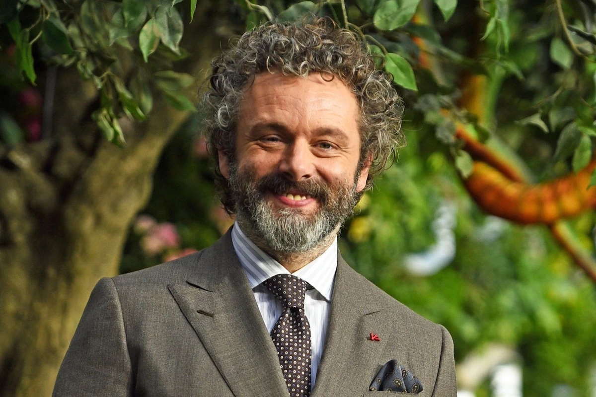 Michael Sheen wearing a grey suit and smiling