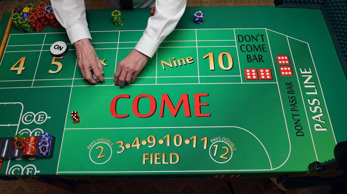 A male dealer’s hands picking chips from a craps table, with a pair of dice showing three and four