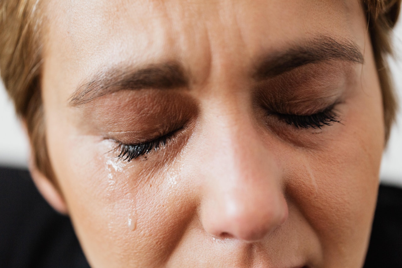A short-haired adult woman shedding tears because of constant pain from trigeminal neuralgia