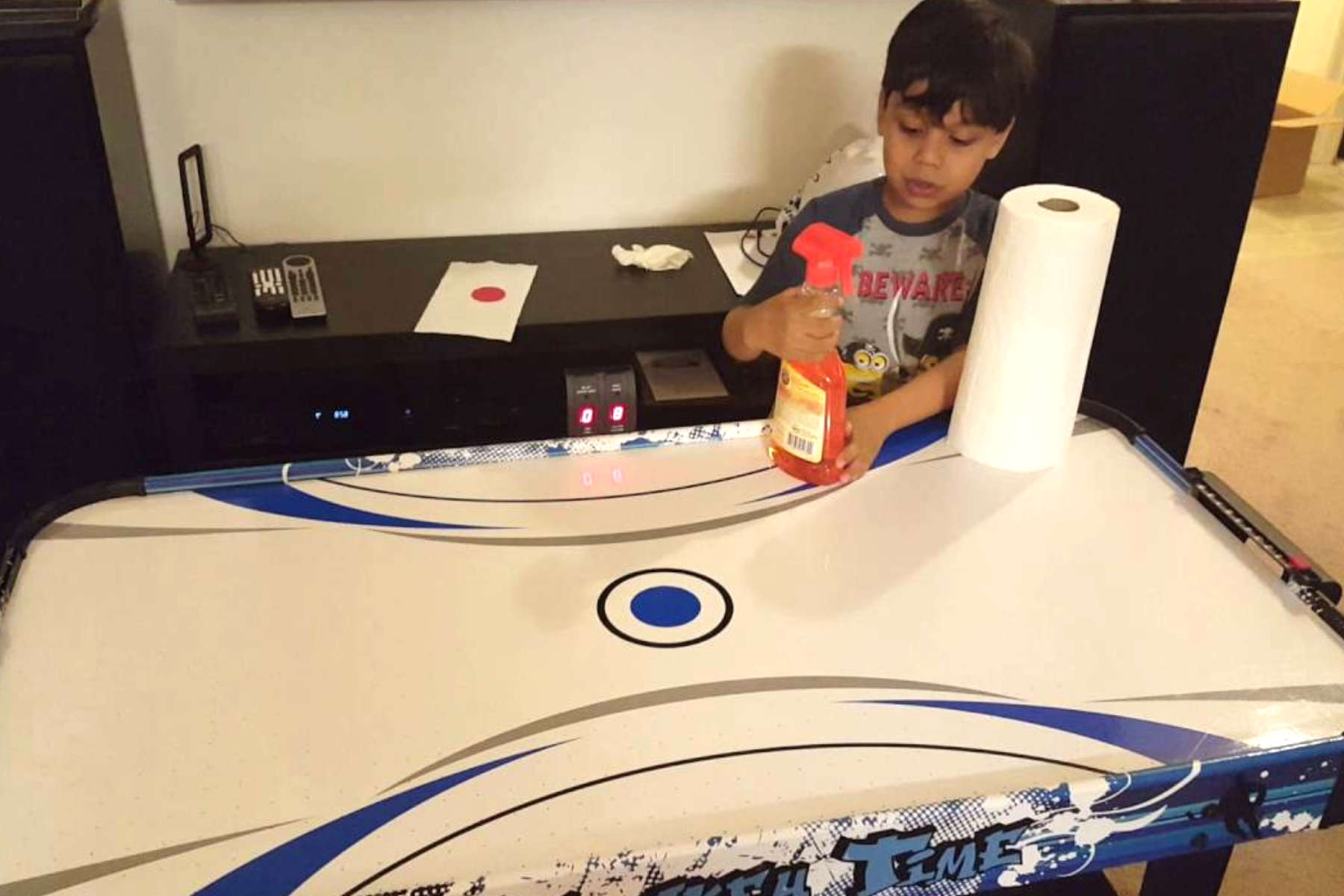 A child is seen wiping the surface of an Air Hockey table with a tissue and safety chemical