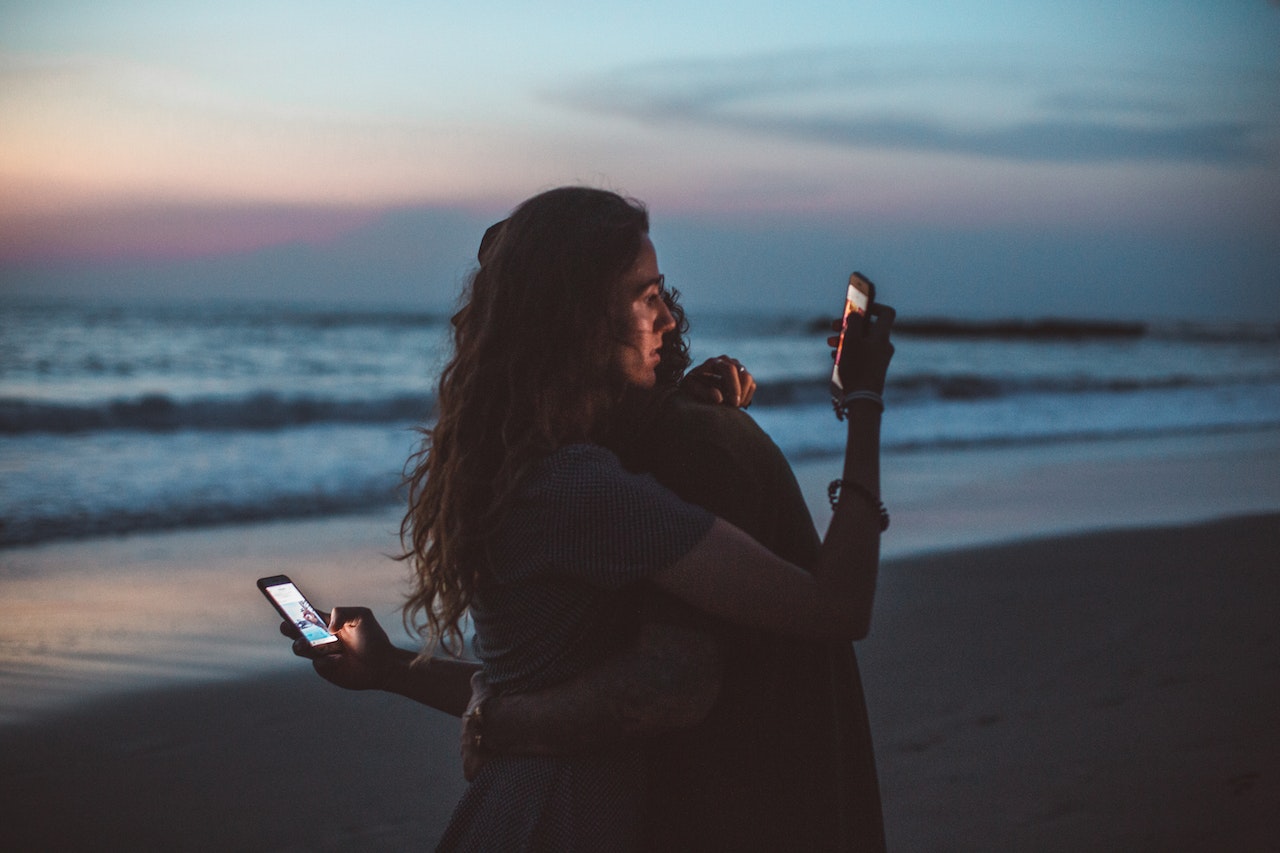 A couple hugging and using smartphone near the sea on sunset