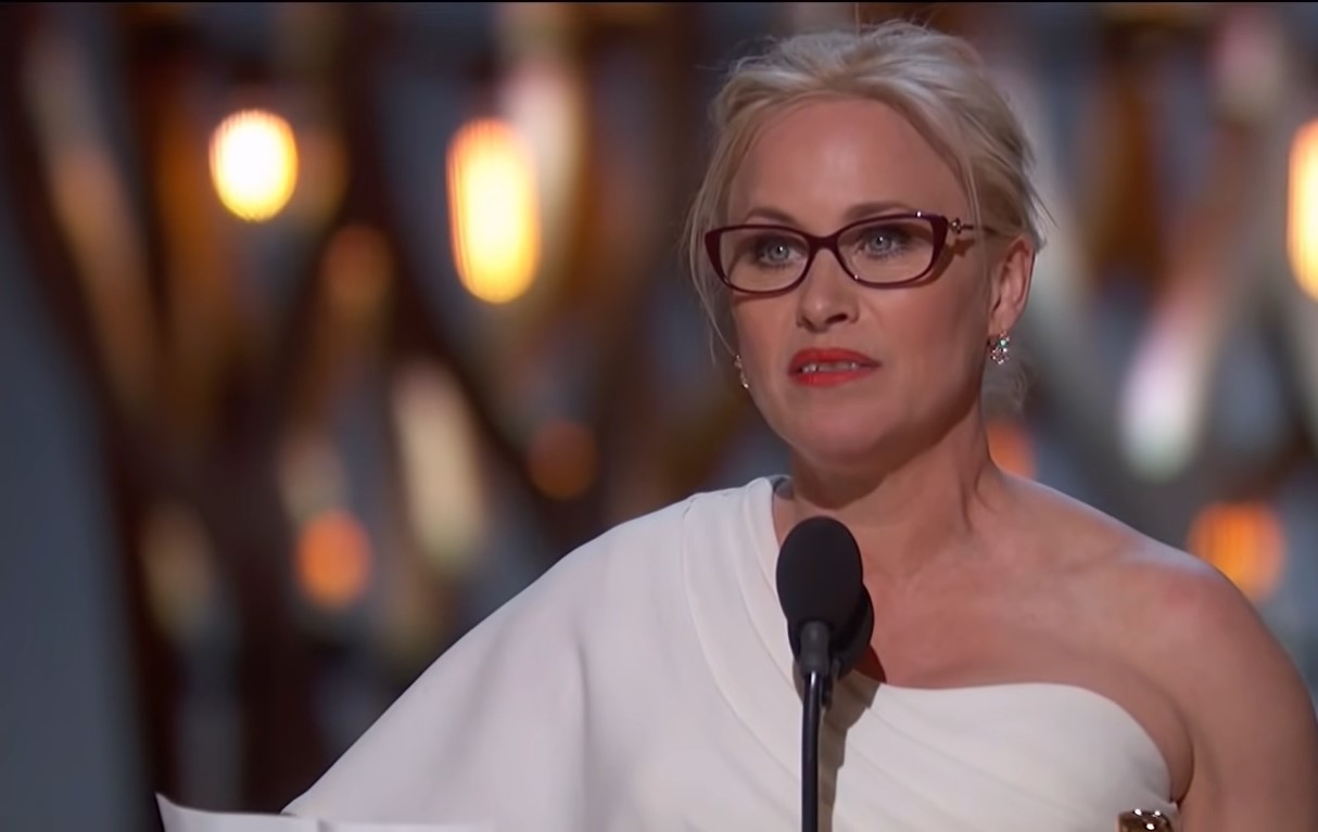 Patricia Arquette in a white one-shoulder dress and reading glasses delivering her acceptance speech at the Oscars