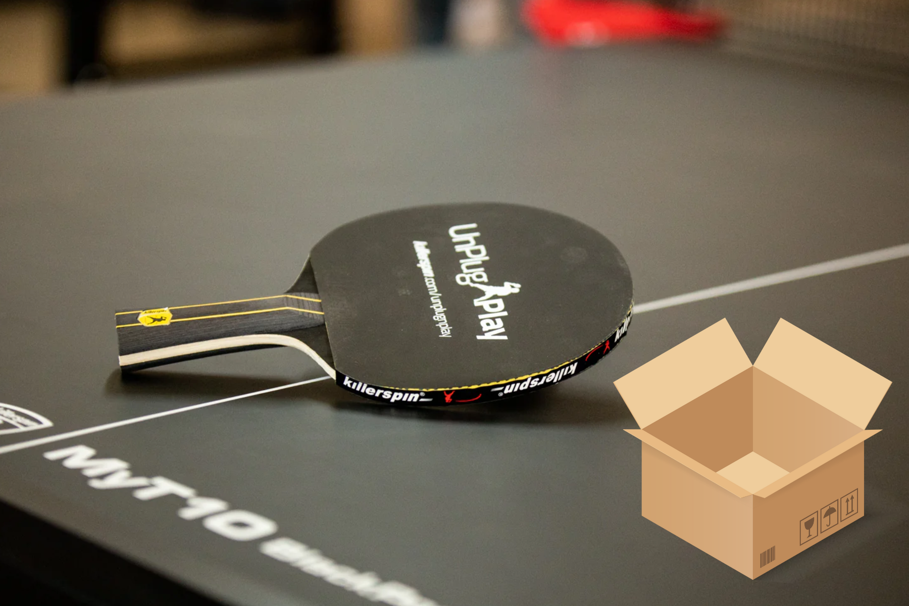 A ping pong paddle rests on a ping pong table beside a small box