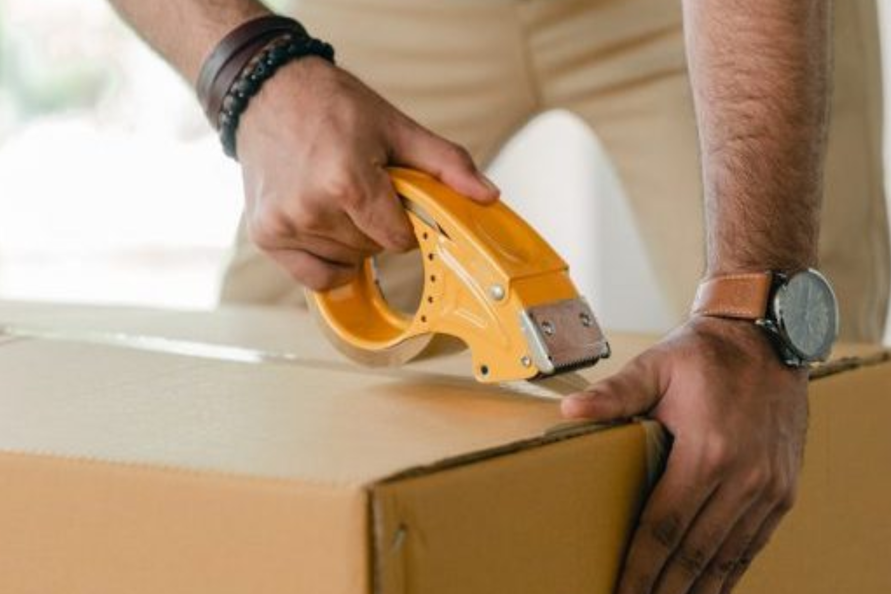 An individual is using packaging tape to seal a box