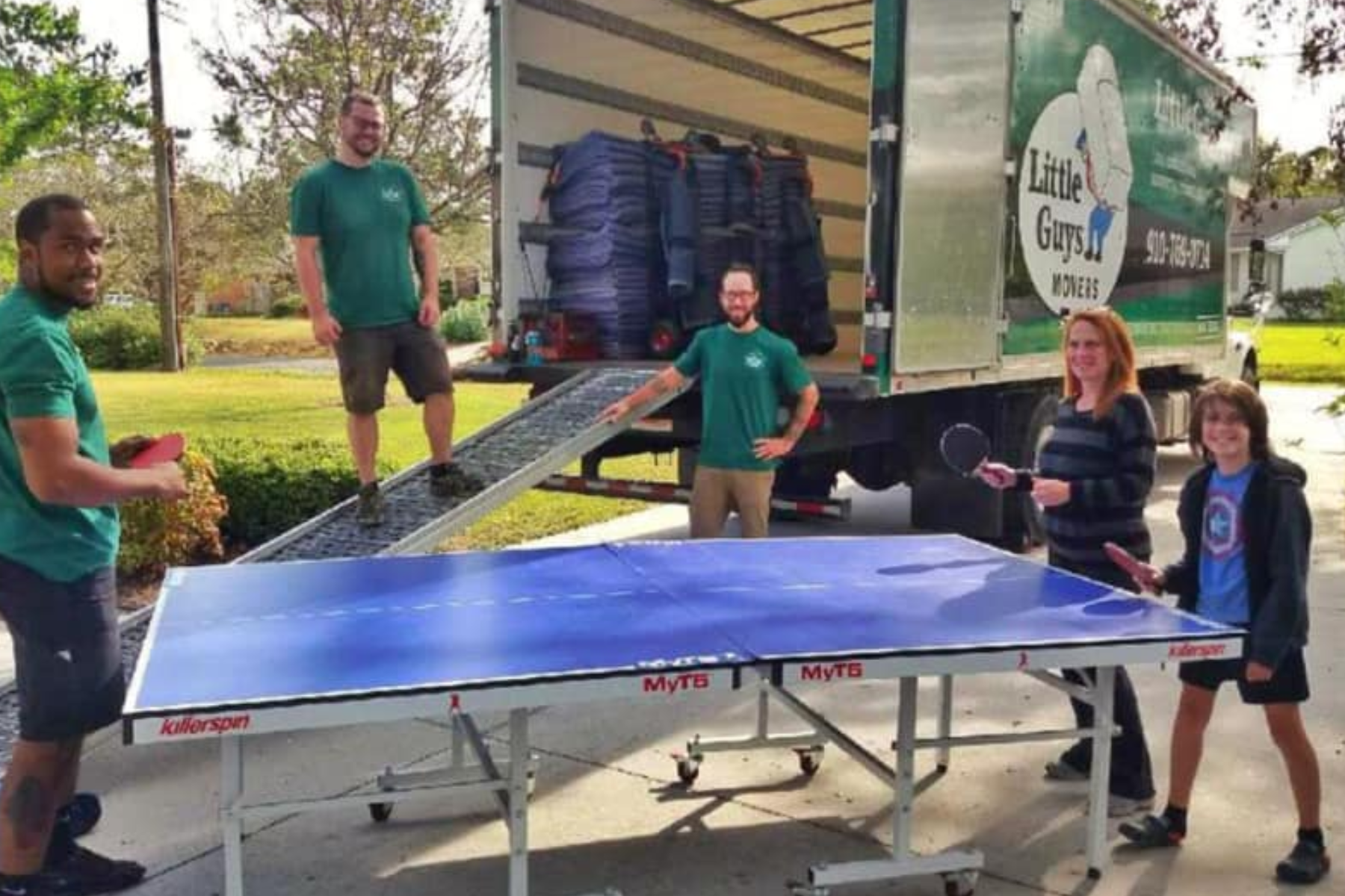 A group of workers from a truck service company are loading a ping pong table onto a truck