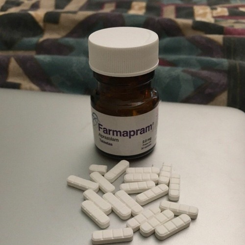 A Farmapram bottle and white rectangualr pills on the white table.