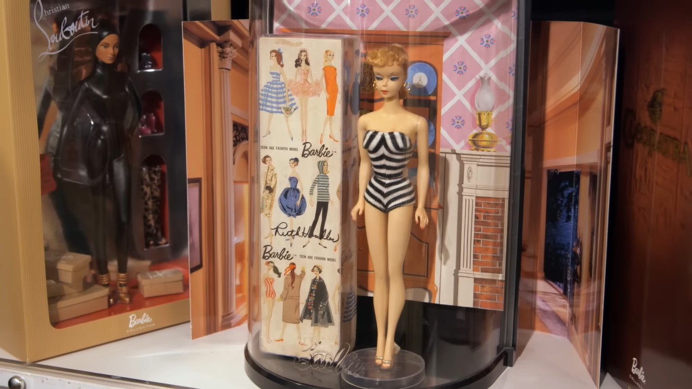 The first Barbie doll in white bathing suit with black stripes inside a plastic container