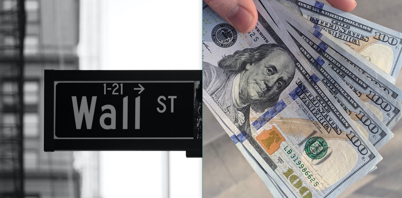 A rectangular Wall Street signage; a hand, with just two fingers shown, holding seven 100-dollar bills