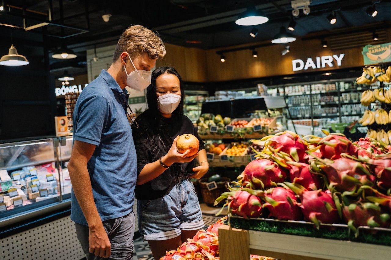 A man and a woman in face mask checking out a fruit near the dairy section of a supermarket