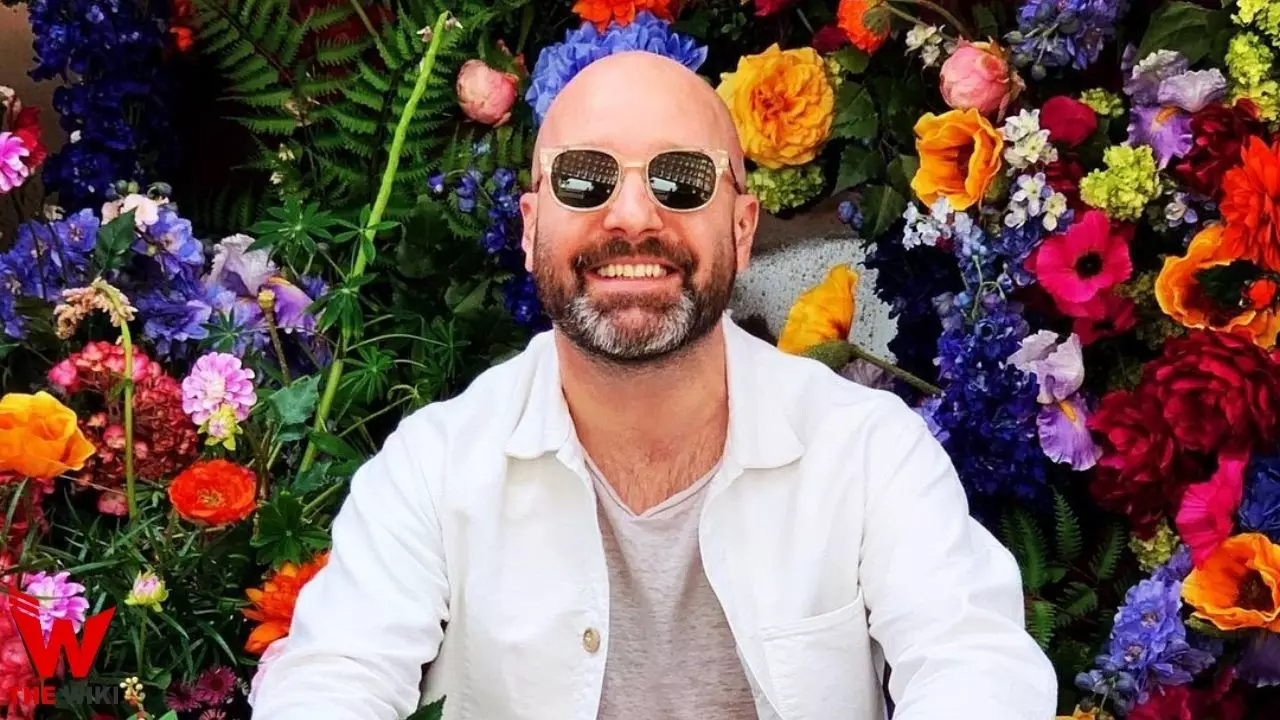 Johnny Harris Posing While Sitting Front Of Flowers