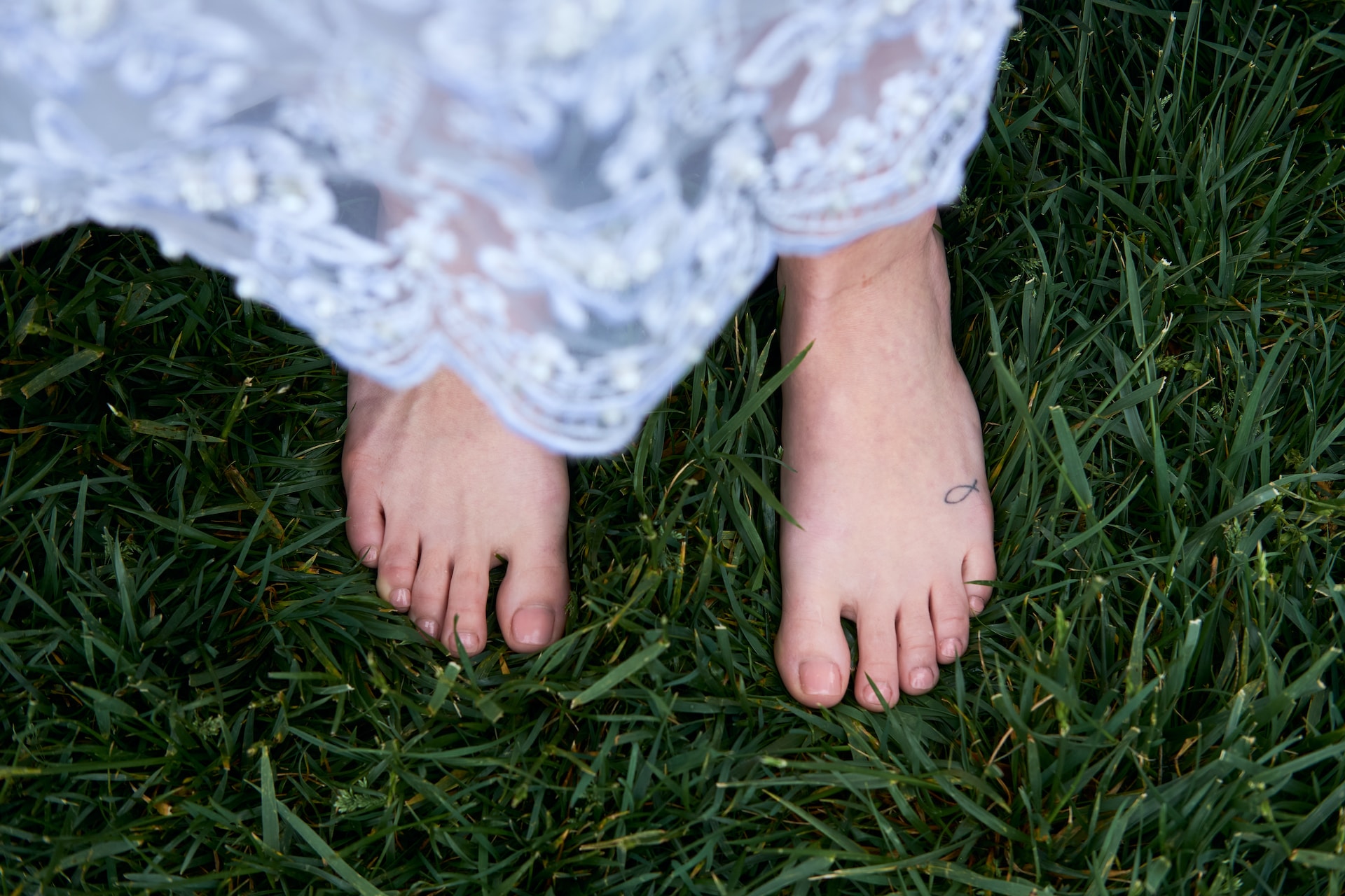 A person with white clothing standing barefoot on the grass.