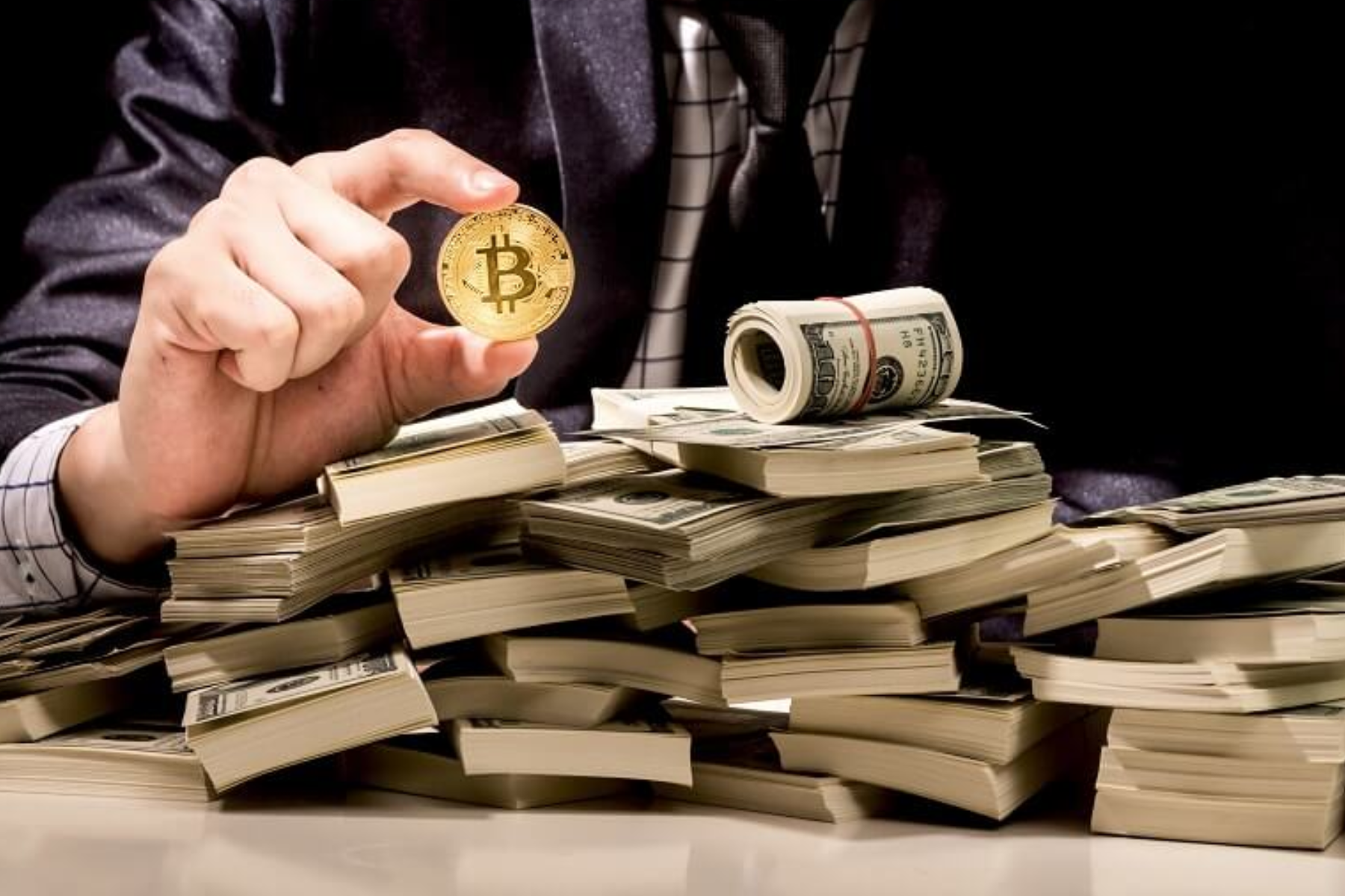 A man holds a bitcoin in front of money on a table