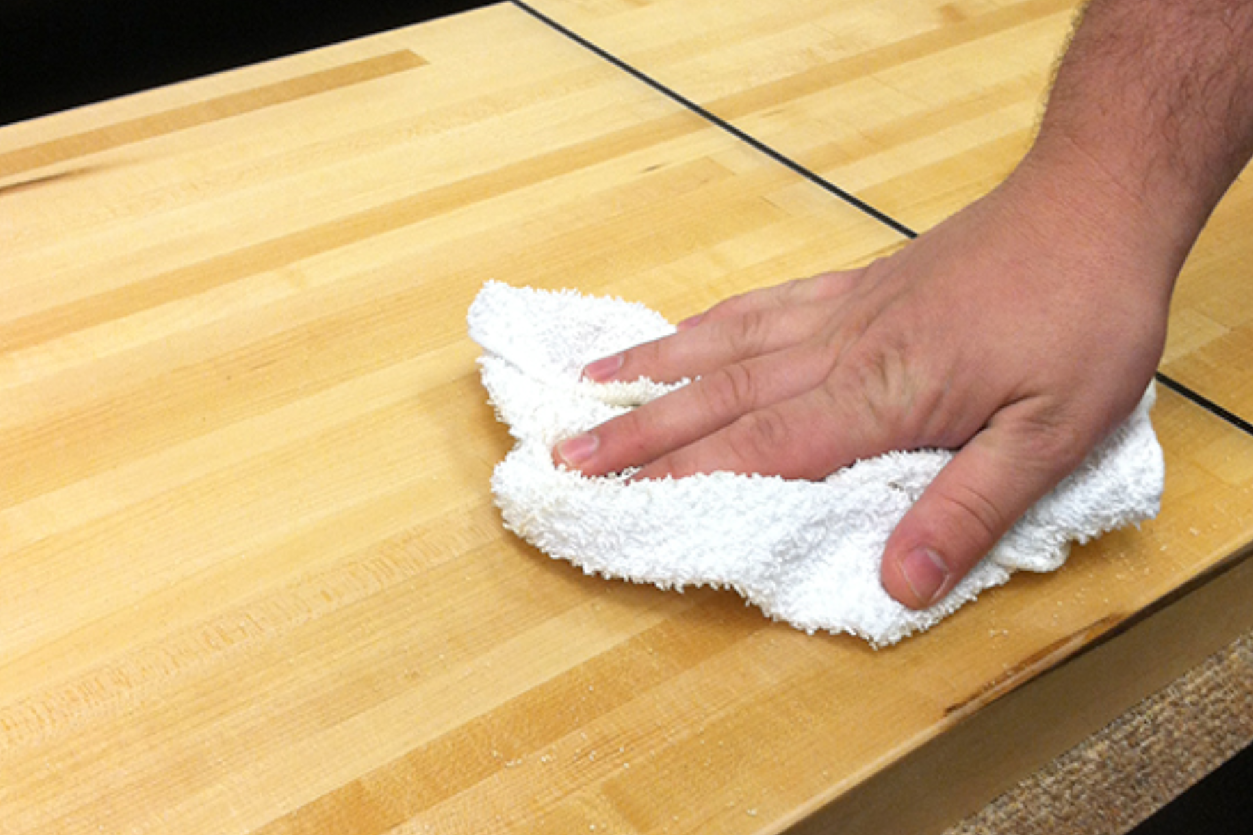 A man's hand washing the surface of a shuffleboard table with a white cloth