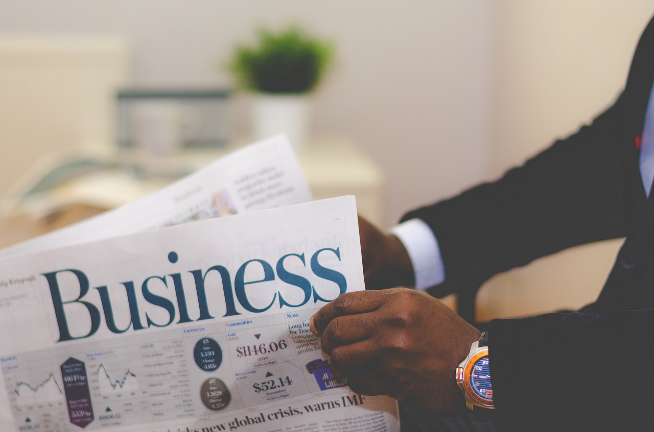 A Black guy in dark suit sitting and opening the Business section of a broadsheet