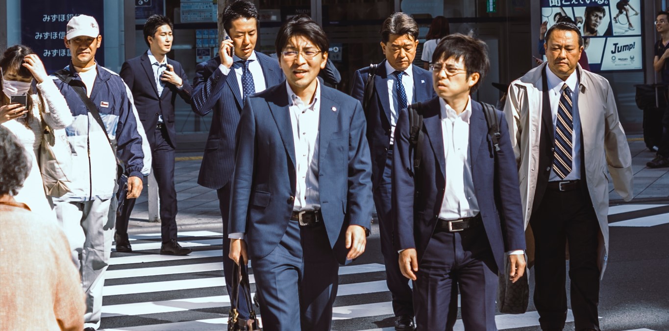Male Japanese office workers in suits walking in the pedestrian crossing at daytime in Shinjuku, Japan
