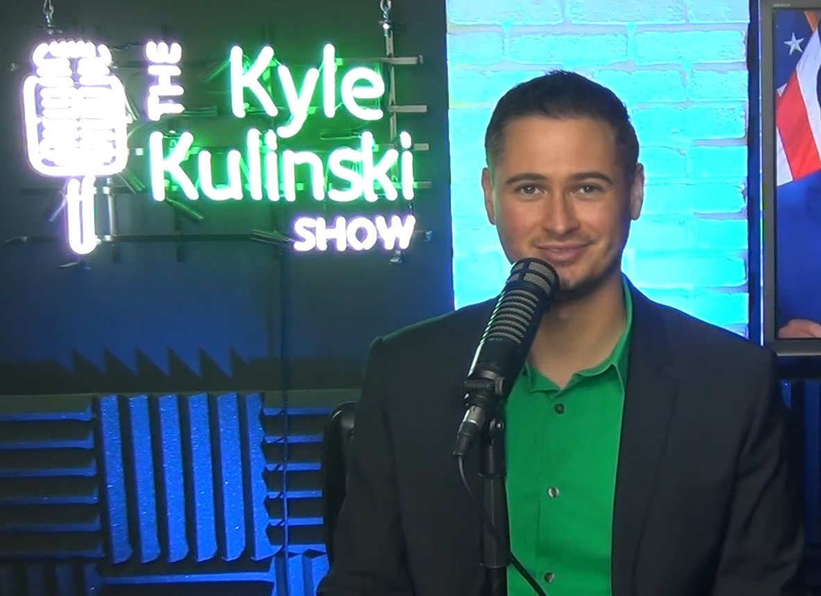 Kyle kulinski sitting in front of camera with the kyle kulinski show written in the background