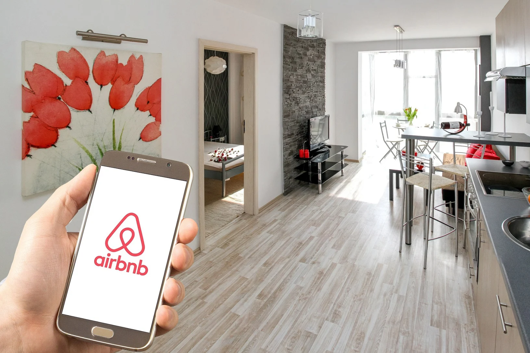 In front of the actual Airbnb, a man's hand holds a phone with the Airbnb logo