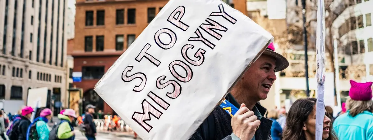 A person in a street crowd holding a sign that says stop misogyny