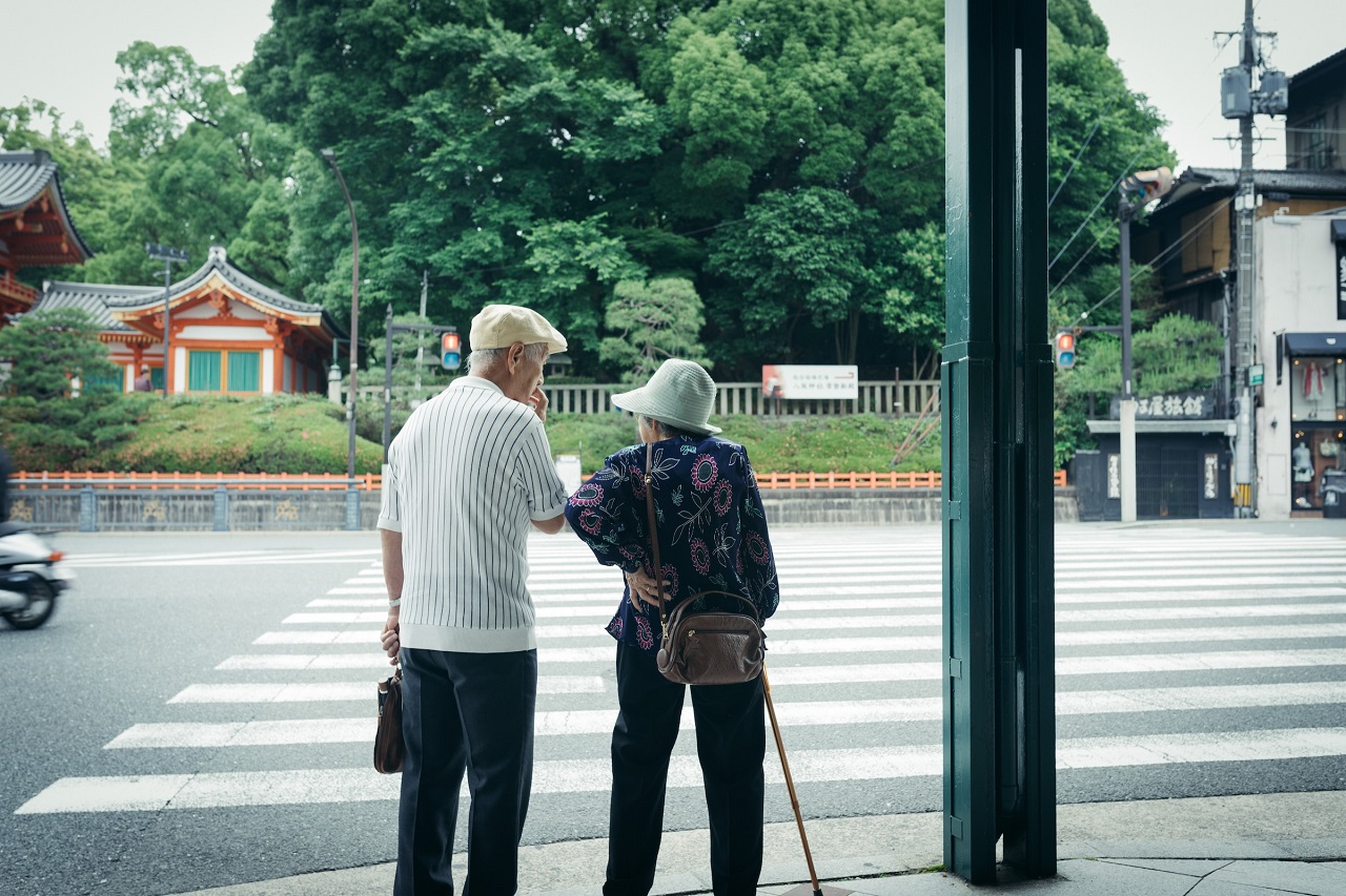 An old Japanese couple wearing hats and standing in front a pedestrian crossing in Kyoto, Japan