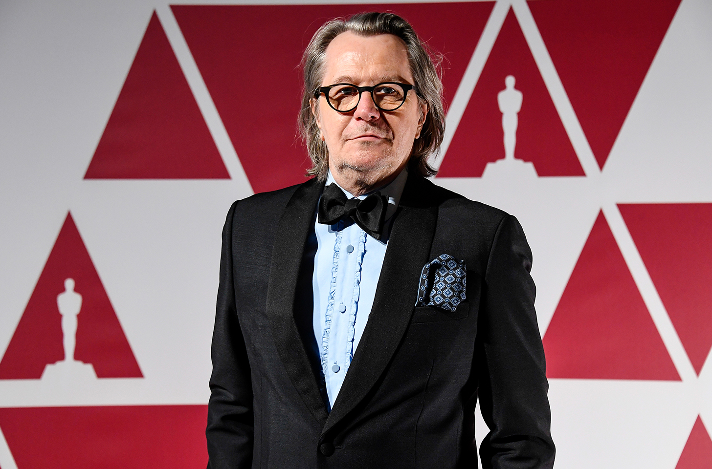 Gary Oldman wearing a black suit and black bow tie