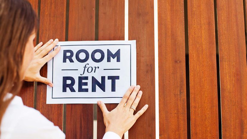 Woman putting a sign of room for rent on wooden door