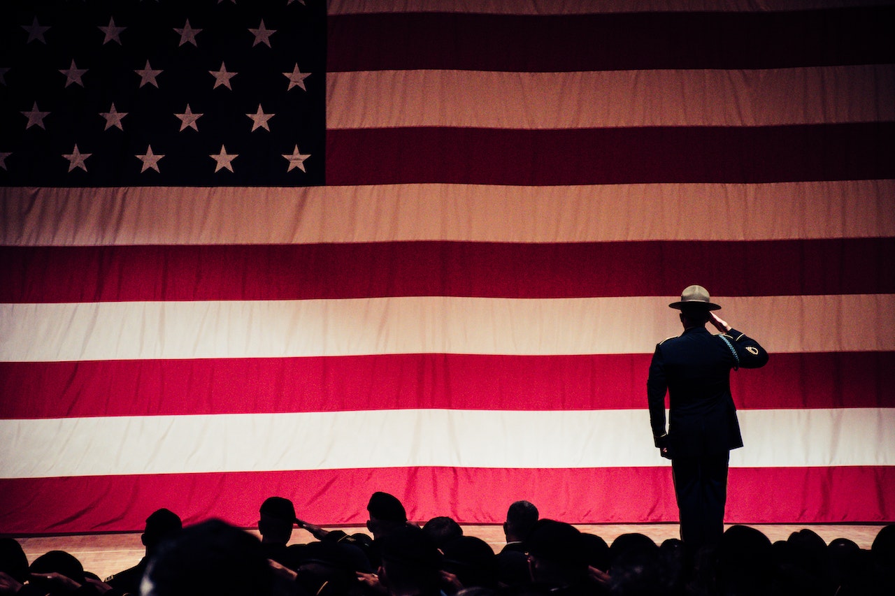 A military officer up on stage saluting to a massive American flag covering the entire wall