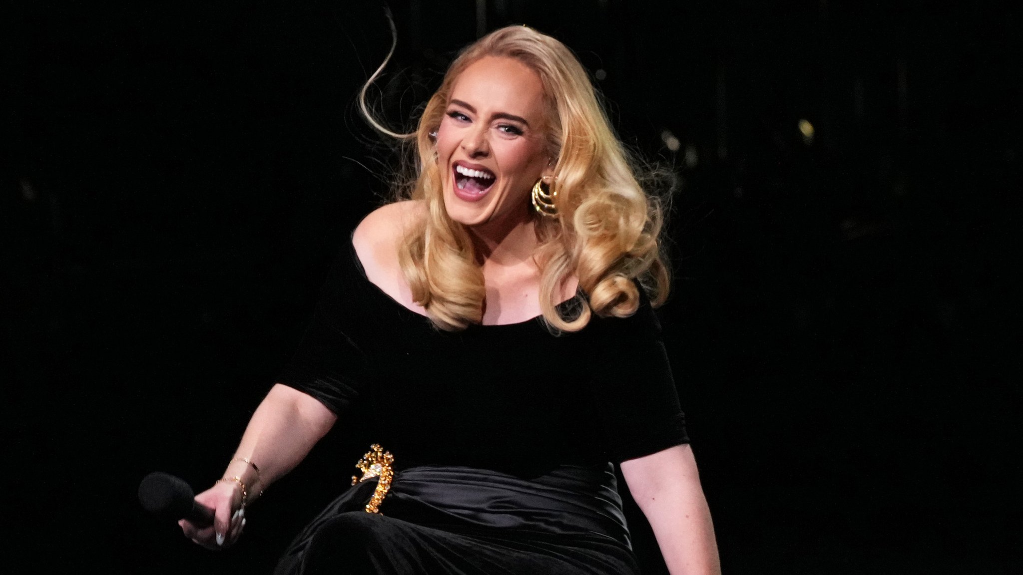 Adele wearing a black dress while holding a mic