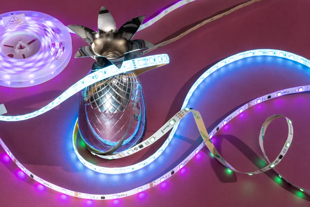 Dynamic arrangement of LED strip lights unfurling around a mirrored disco ball, creating a playful interplay of light and reflections on a pink surface.