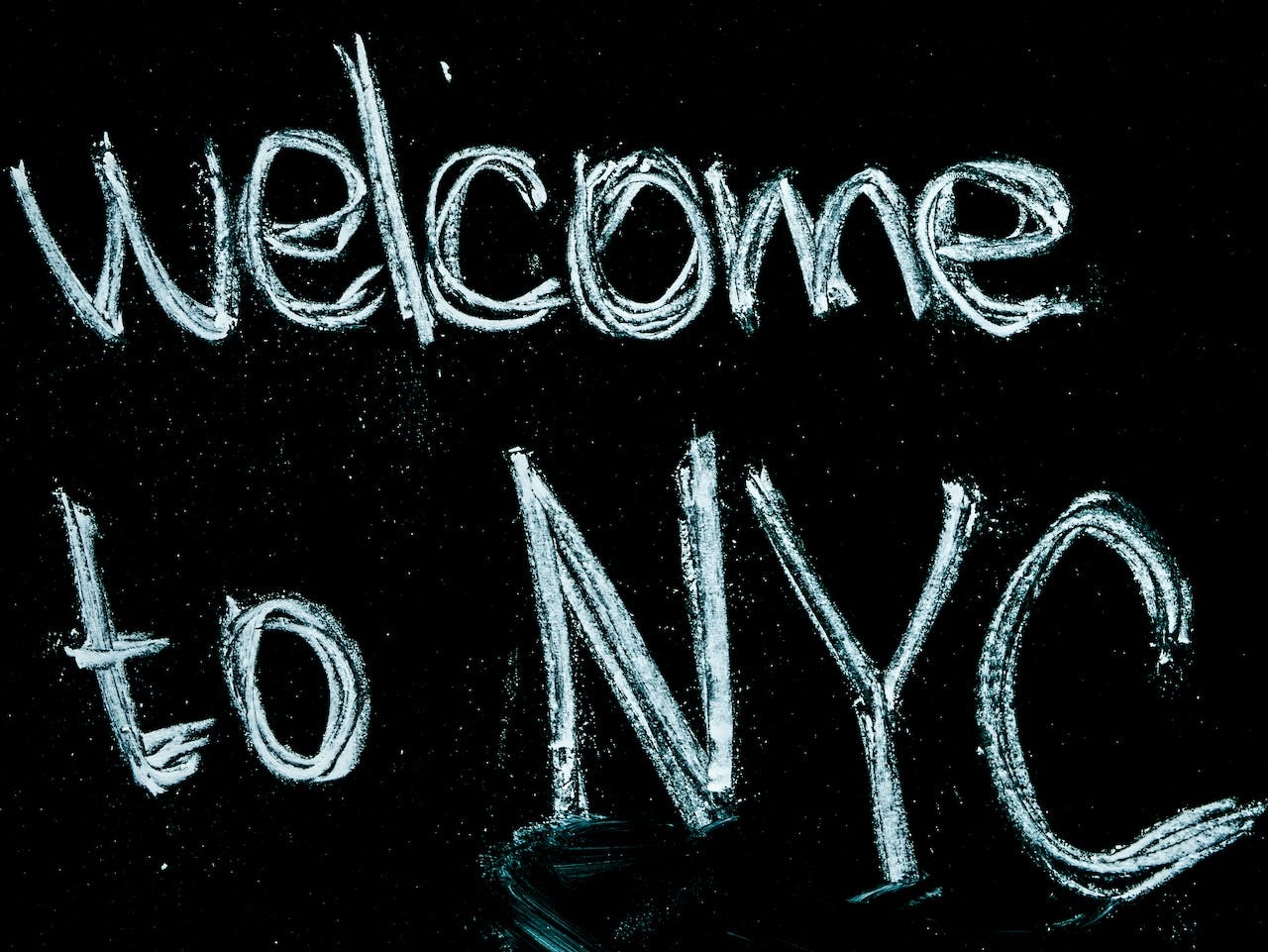 A handwritten ‘welcome to NYC’ sign in white chalk and thick lettering on a black background