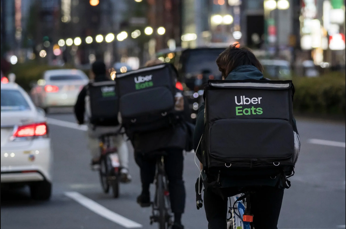 A group of people riding bicycles down a city street with Uber Eats bags on their backs. 