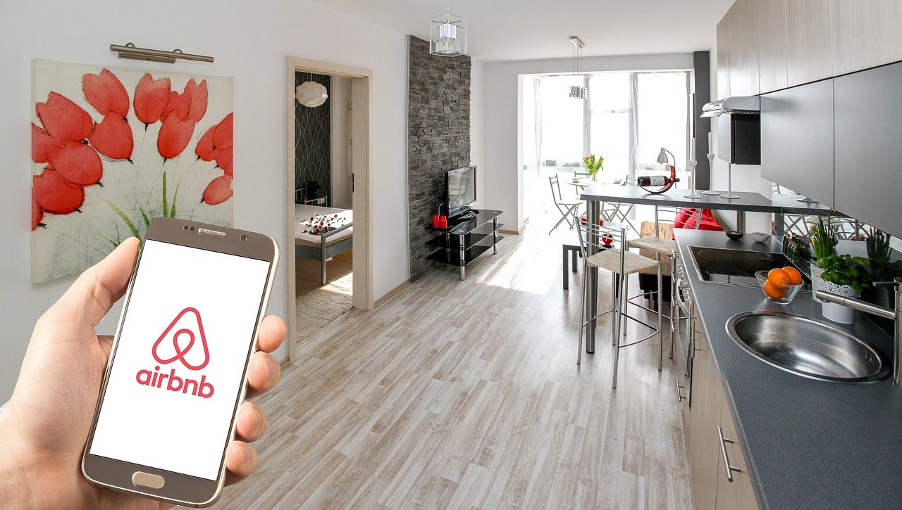 A hand holding a smartphone with Airbnb name and logo on it in a one-bedroom apartment