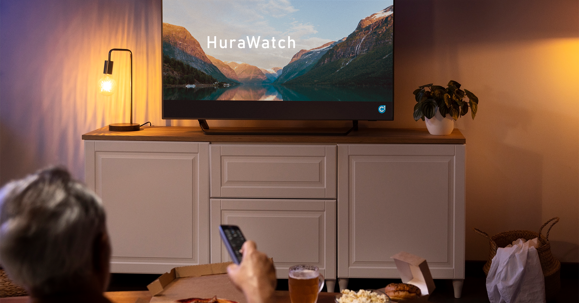 A person in a cozy living room setting, using a remote to access "HuraWatch" on a large screen TV.
