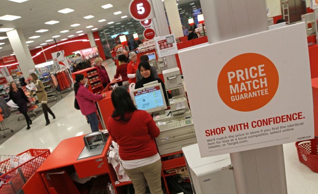 A woman checking out at a store with a price match guarantee sign.