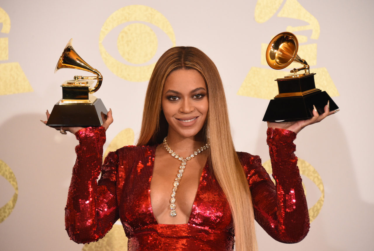 Beyoncé wearing a red dress while holding two Grammys