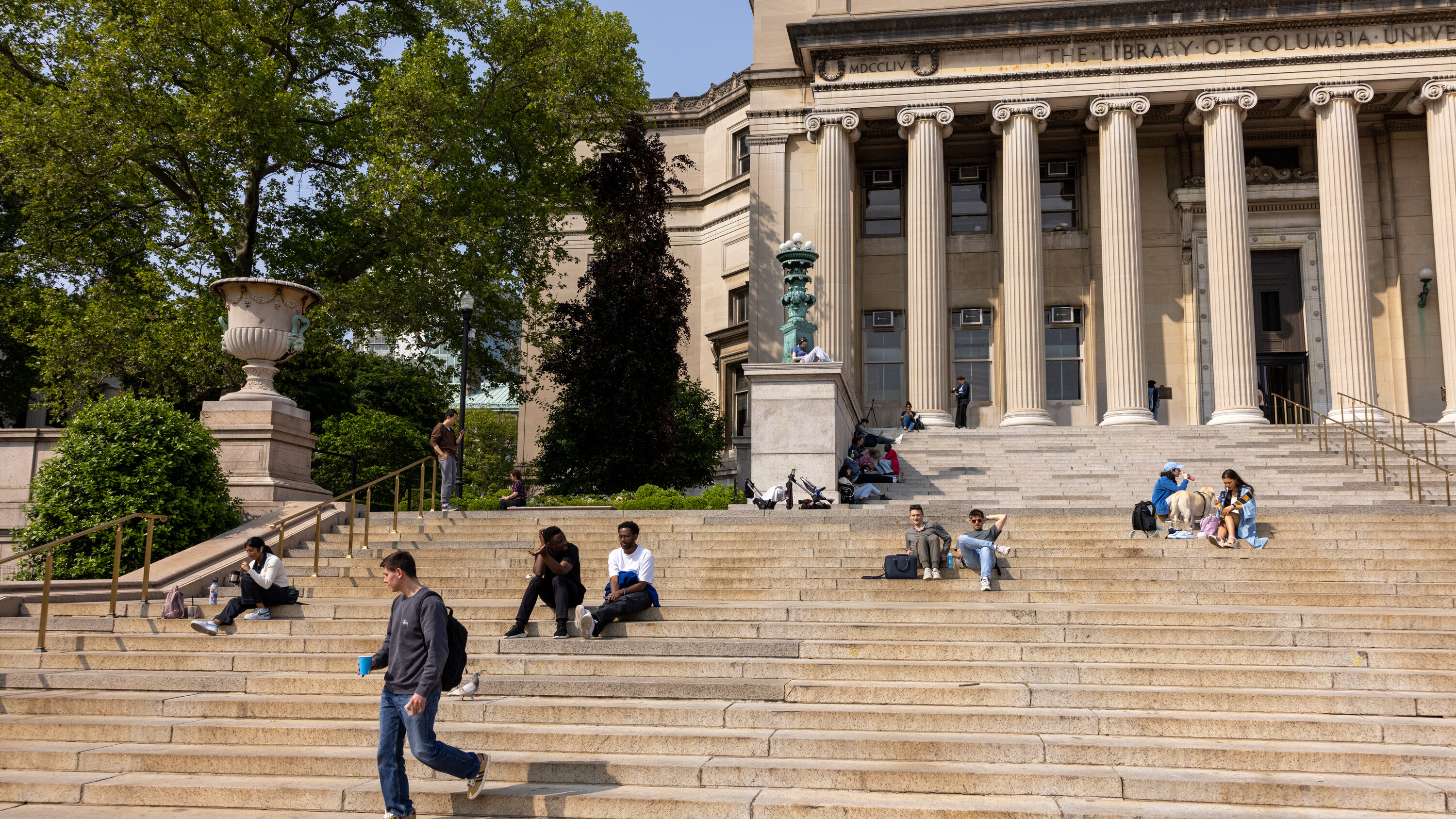 Visitors relax on the grand steps outside the iconic library of Columbia University on a sunny day.