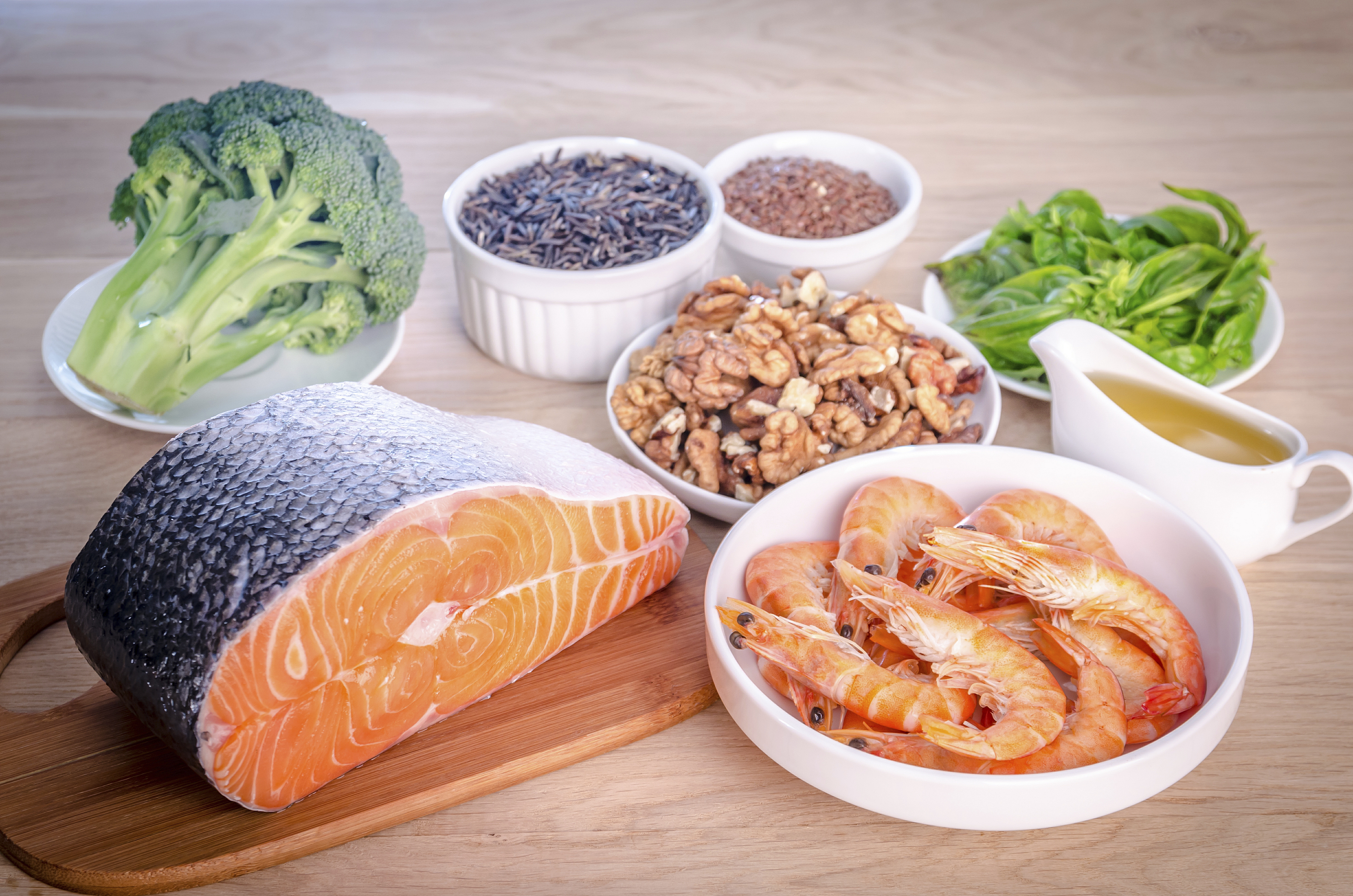 Healthy foods, including a salmon fillet, shrimp, nuts, wild rice, broccoli, spinach, and olive oil, representing a balanced diet rich in proteins, omega-3 fatty acids, and greens.